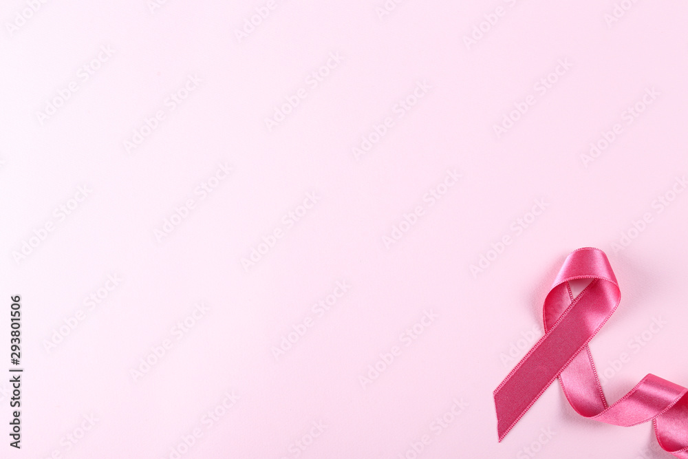 The pink colored ribbon - international symbol of breast cancer awareness and moral support for women. Paper textured background, copy space, close up, top view fat lay.