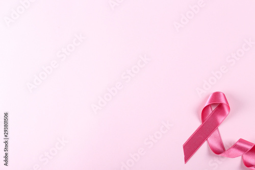 The pink colored ribbon - international symbol of breast cancer awareness and moral support for women. Paper textured background, copy space, close up, top view fat lay.