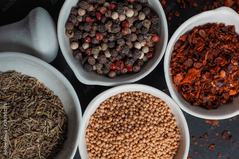 Paprika, mustard, caraway seeds and a mixture of peppercorns in white ceramic bowls next to the mortar isolated on black background Paprika, mustard, caraway seeds and a mixture of peppercorns in white ceramic bowls next to the mortar isolated on black background