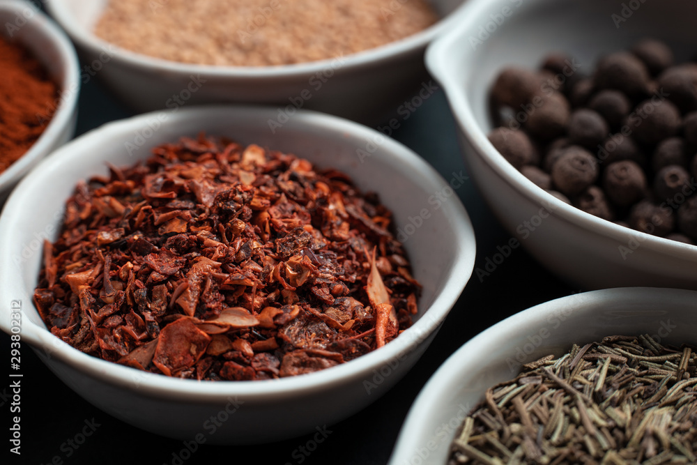 Paprika, mustard, caraway seeds and a mixture of peppers in white ceramic bowls next to the mortar isolated on black background Paprika, mustard, caraway seeds and a mixture of peppers in white ceramic bowls next to the mortar isolated on black background
