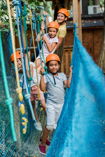 selective focus of cheerful multicultural kids in helmets near ropes