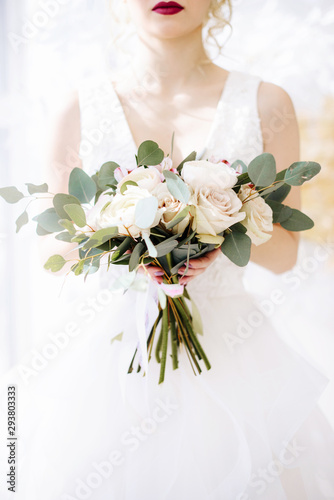 The bride holds in hands a beautiful wedding bouquet. Portrait of an elegant bride with professional makeup and hairstyle in a luxurious wedding dress. Wedding details and accessories, rustic wedding