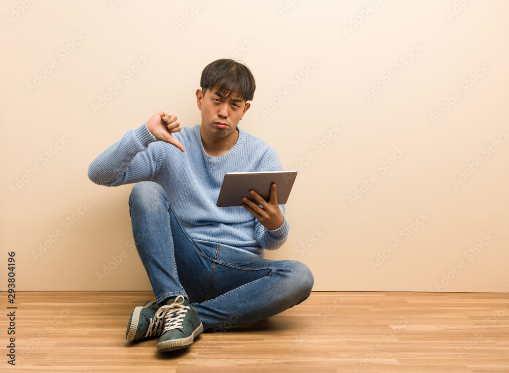 Young chinese man sitting using his tablet pointing fingers, example to follow