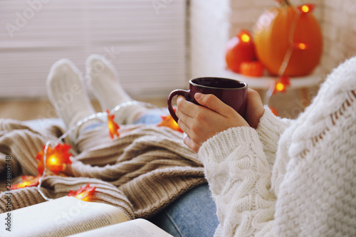 Top view of woman relaxing on couch at home, drinking latte. Cozy evening at home. Young woman enjoying alone time, sitting on sofa covered with soft blanket. Close up, copy space.