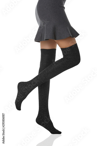 Medium bottom shot of a female figure in the gray bell-shaped skirt and black shadow-proof stockings with lurex. The girl on tiptoe is posing on the white background.  photo