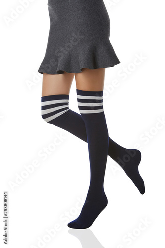 Medium bottom shot of a female figure in the gray bell-shaped skirt and deep blue shadow-proof stockings with three white stripes on the top. The girl on tiptoe is posing on the white background.  photo