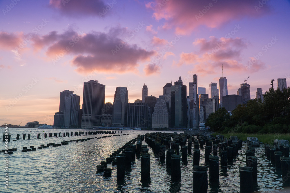 Beautiful wide view of downtown Manhattan skyline financial district as sun goes down in majestic sunset behind city cast purple color across evening sky