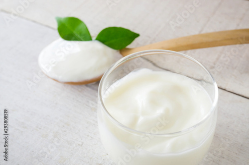 Yogurt cup and spoon on white wood background.