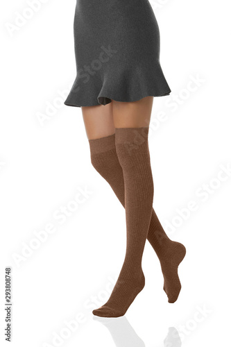 Medium bottom shot of a female figure in the gray bell-shaped skirt and beige shadow-proof ribby stockings with closely rim on the top. The girl on tiptoe is posing on the white background.  photo