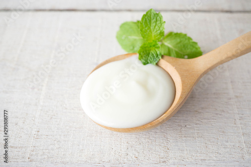 White yogurt with mint leaf on wooden spoon on white wood background.