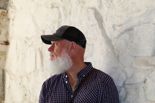Man in cap and beard against white stone wall