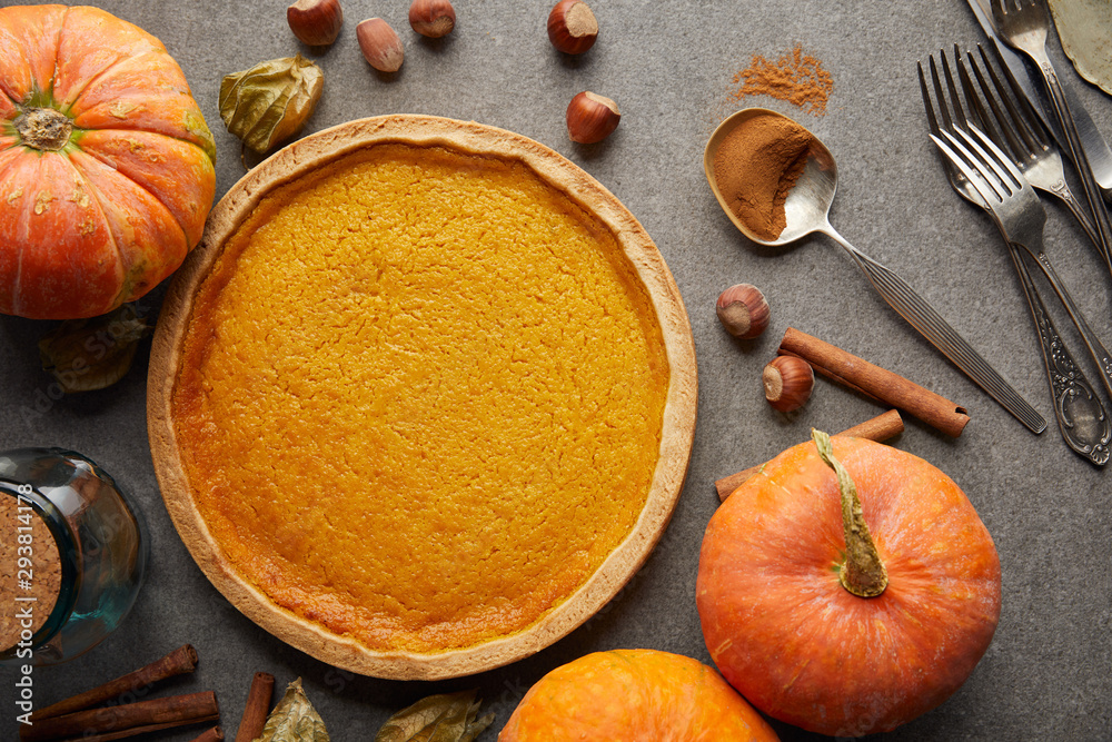 top view of delicious pumpkin pie near whole pumpkins, cutlery and hazelnuts on grey stone surface top view of delicious pumpkin pie near whole pumpkins, cutlery and hazelnuts on grey stone surface