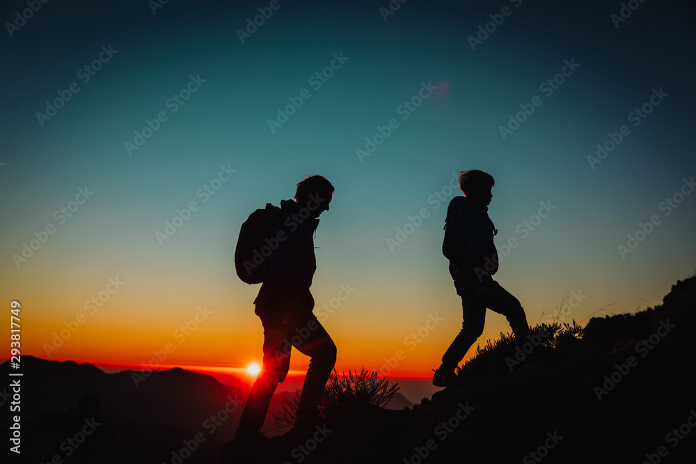 Silhouettes of father and son hiking in mountains at sunset