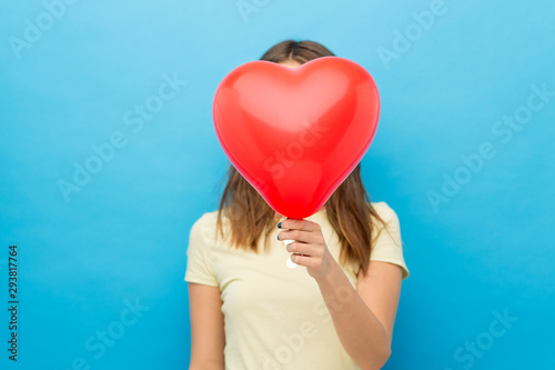 valentine s day and people concept - young woman covering face with heart-shaped balloon over blue background