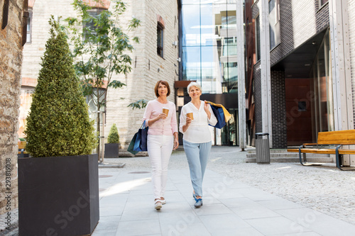 sale, consumerism and people concept - two senior women or friends with shopping bags drinking takeaway coffee and walking along tallinn city street