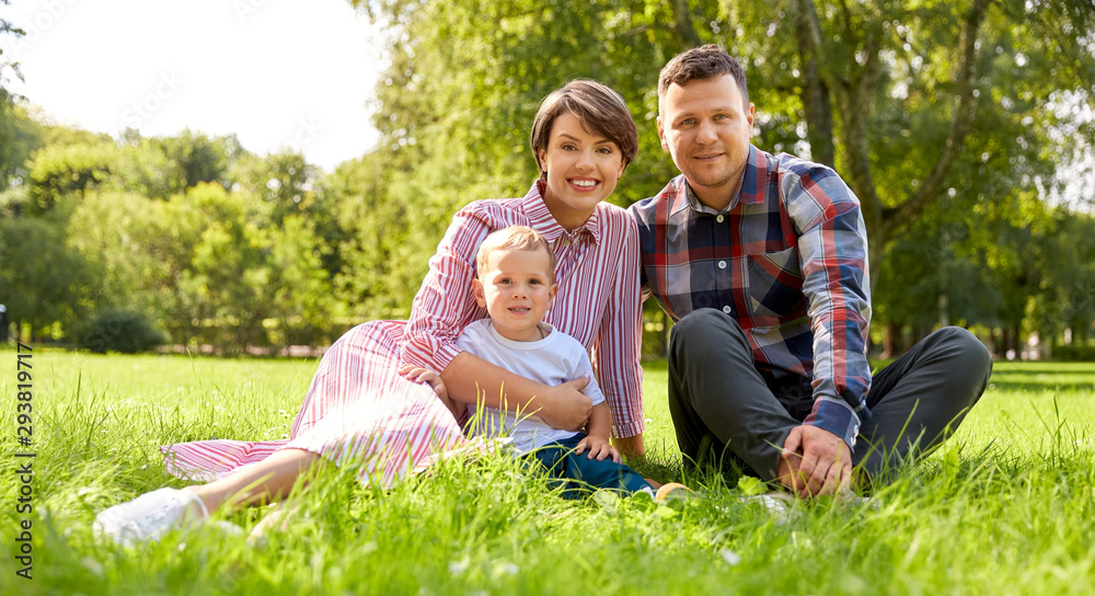 Fototapeta premium family, leisure and people concept - happy mother, father and little son at summer park sitting on grass