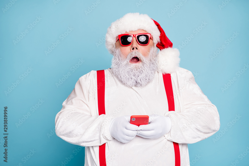 Close up photo of amazed funny funky overweight white hair long bearded santa claus hipster use cell phone search winter discount text sms wear red suspenders isolated over blue color background - obrazy, fototapety, plakaty 