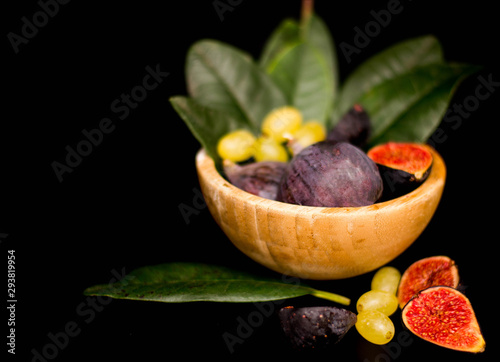 Fresh figs in a wooden plate, with grapes and leaves, shot low key. Vintage, close-up, top view.