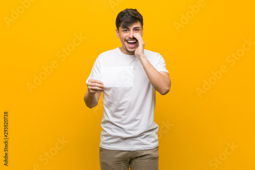 Young hispanic man holding a placard shouting excited to front.