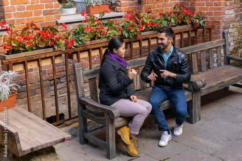 young man and woman are having fun discussing something while sitting on a bench outdoors