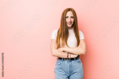 Young redhead ginger woman against a pink wall laughing and having fun.