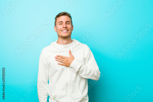 Young caucasian sport man laughs out loudly keeping hand on chest.