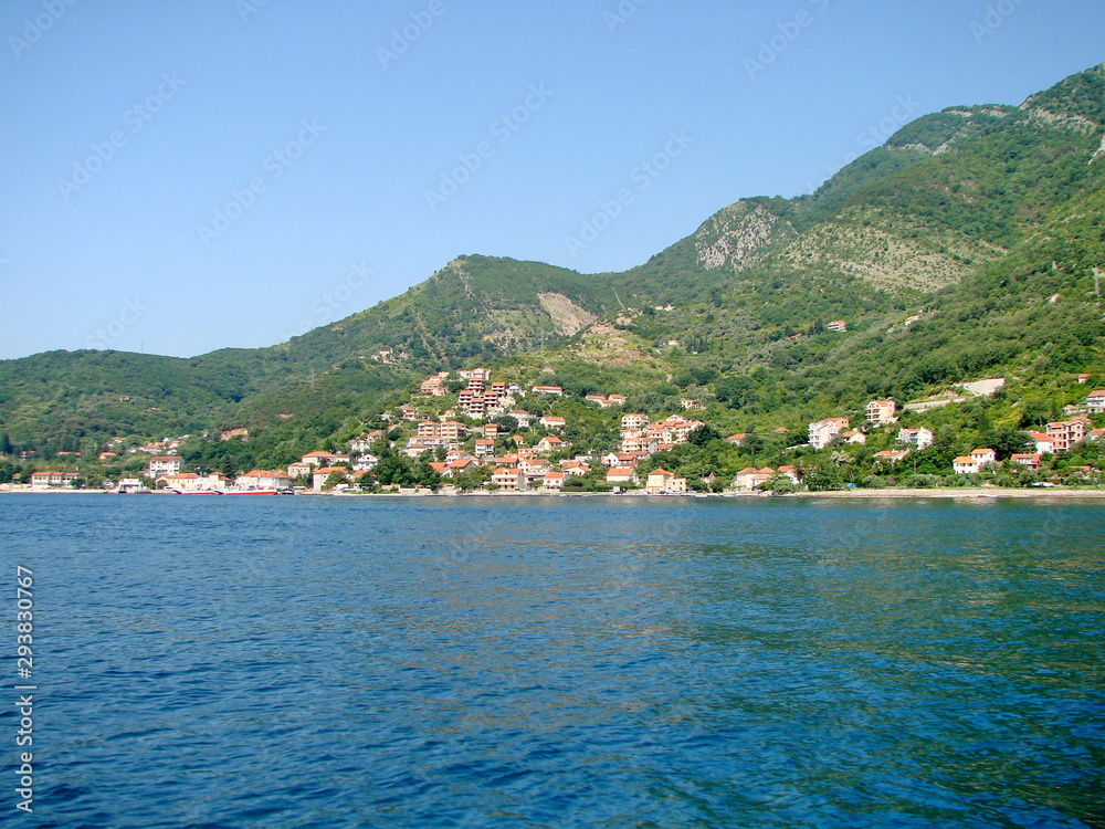 View from the sea to the coastal town of Montenegro at the foot of the hill reflected on the azure sea surface.