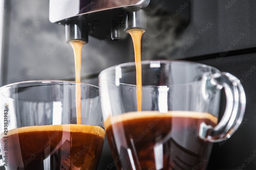 freshly brewed coffee is poured from the coffee machine into glass cups