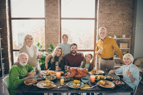 Photo of big family sitting hugging feast table holiday roasted turkey making portrait eight relatives wife husband multi-generation raise wine glasses in living room indoors