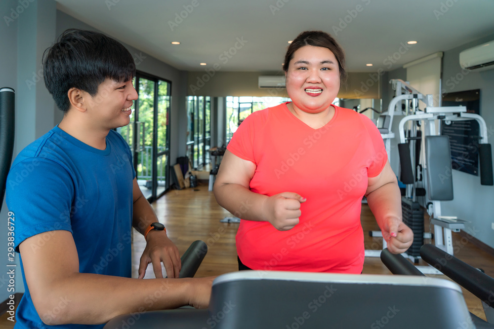 Two Asian trainer man and Overweight woman exercising training on treadmill in gym, trainer looking happy her result during workout. Fat women take care of health and want to lose weight concept..