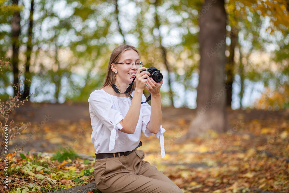 Attractive beautiful young girl holding modern mirror-less camera in autumn park.