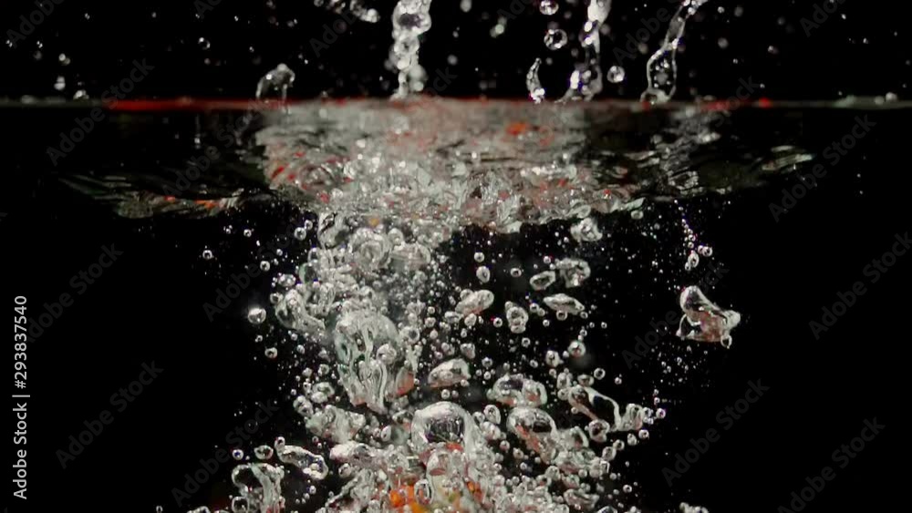 Cherry tomatoes splashing into water on black background closeup in super slow motion
