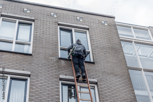 Window cleaner on a ladder cleaning the windos high against a building of brick walls.