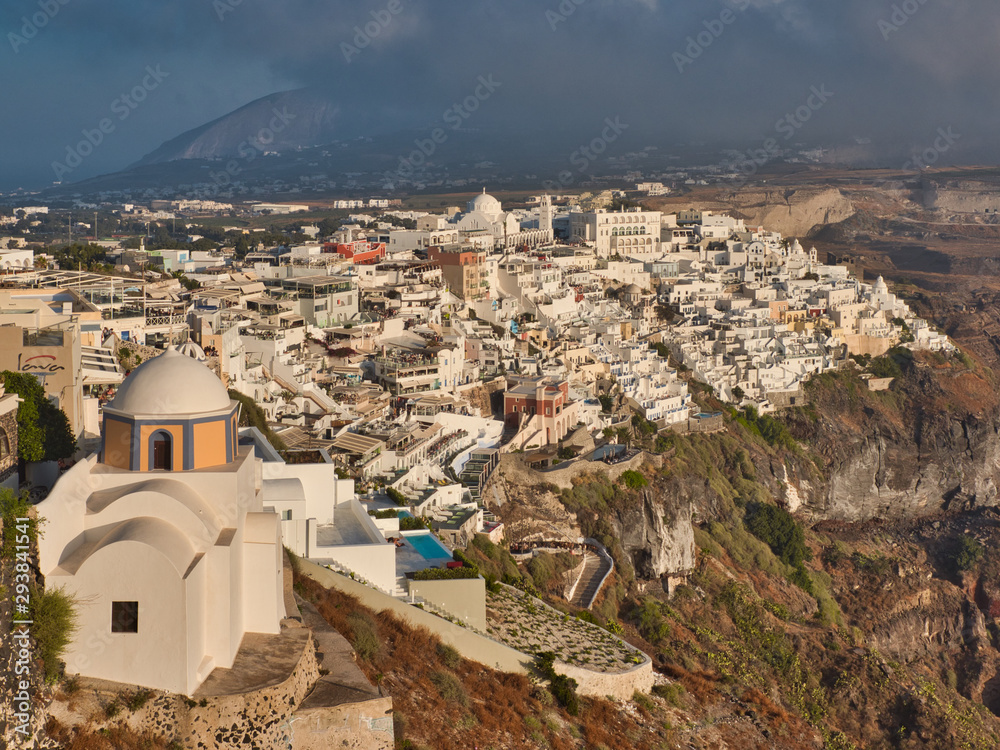 From above breathtaking view of Fira capital of Santorini with stone church and houses on cliffs during storm in Greece