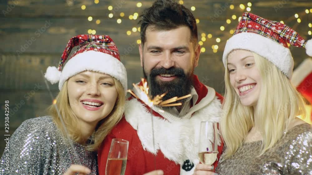Celebrating New Year or Christmas together. Group of beautiful young people in Santa hats lit sparklers and drank champagne looking happy. Merry Christmas and Happy New Year. Man with blondes New Year Celebrating New Year or Christmas together. Group of beautiful young people in Santa hats lit sparklers and drank champagne looking happy. Merry Christmas and Happy New Year. Man with blondes New Year