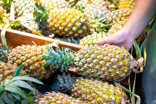 Hand picking up a pineapple from the wooden tray in fresh market photo