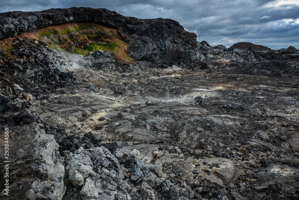 Leirhnjukur old black lava field with fumes coming from ground and blue sky in Iceland, overcast day in summer , film effect with grain Leirhnjukur old black lava field with fumes coming from ground and blue sky in Iceland, overcast day in summer , film effect with grain