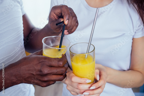 international couple in love holding in hands glasses with orange juice.afro man use disposable tableware,but european woman useing eco steel tubes