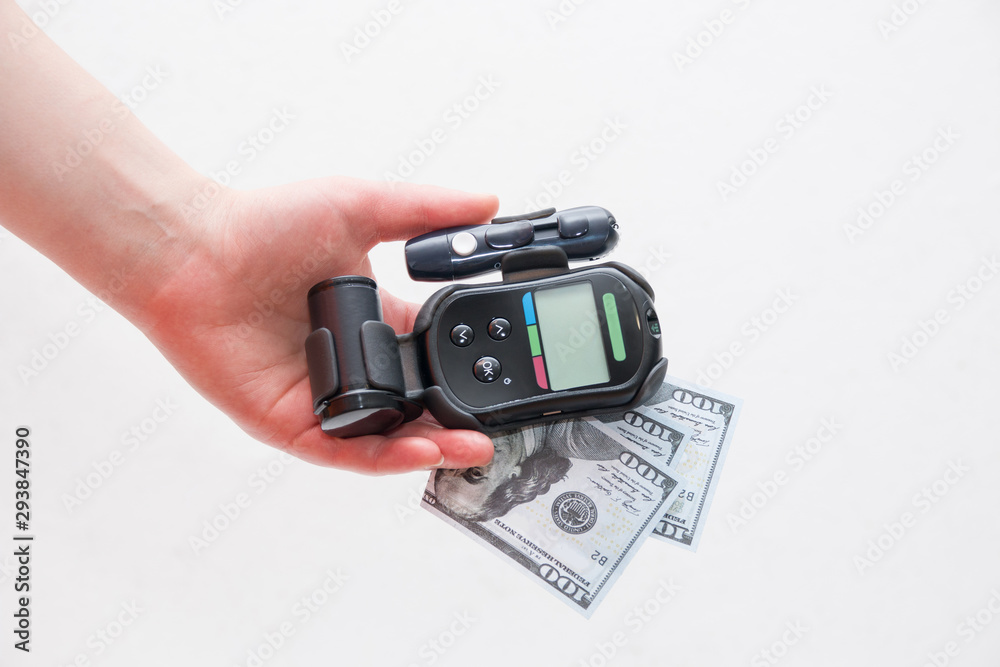 female hand holds a black glucometer and several notes of 100 dollars, white background female hand holds a black glucometer and several notes of 100 dollars, white background