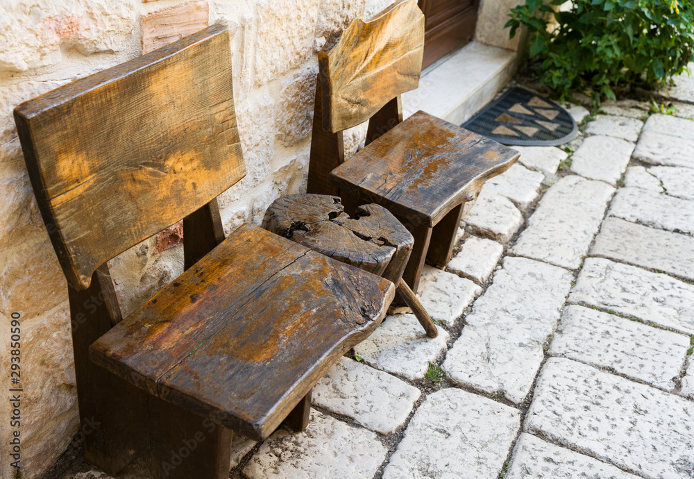 Fragment of the street in the old city. Two small chairs and a wooden table stand against the white stone wall. Selective focus. Copy space.