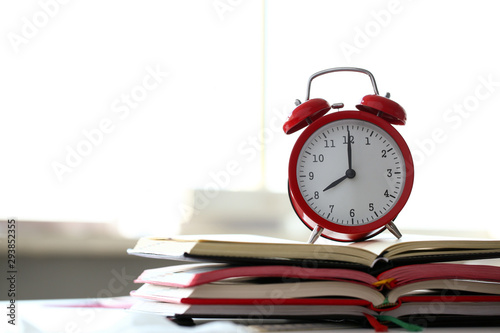 Red alarm clock set at eight in the morning closeup standing on pile of books. Business or education concept