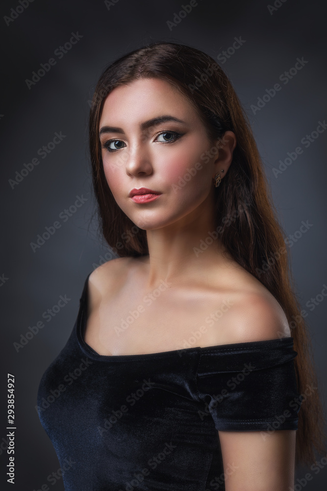 Naklejka premium Portrait of a young beautiful girl in a black dress, close-up. Model with dark hair posing near the wall