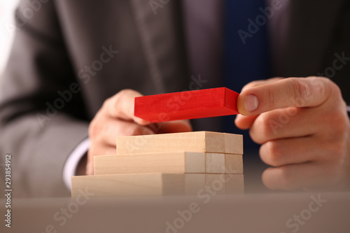 Male hand holds red wood block of stair finish next step rare progress personnel talent authority hot pyramid background on ladder different insurance concept closeup