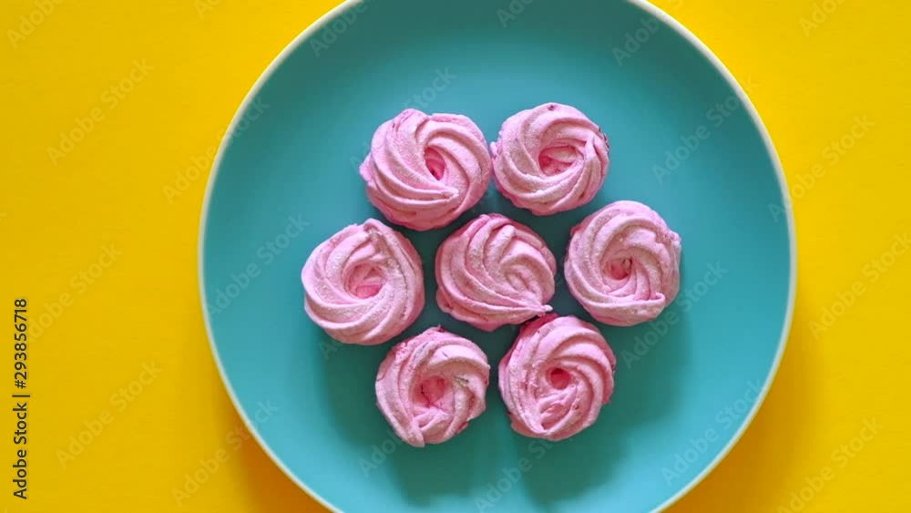 Appetizing sweet desserts rotate 360 on a blue plate on yellow background. Handmade pink marshmallows. Top view.