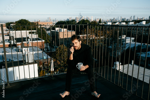 Attractive young man taking a coffee from a rooftop with the New York skyline from behind photo