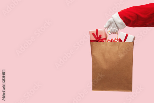 Santa Claus hand holding brown shopping bag with gift boxes