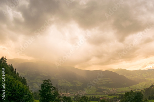 Thunderstorm over a mountain is illuminated from behind by the sun at sunset © Menyhert