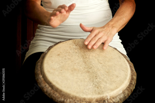 Woman's hands in motion as she drums on top of goat skin covered drum against dark background.