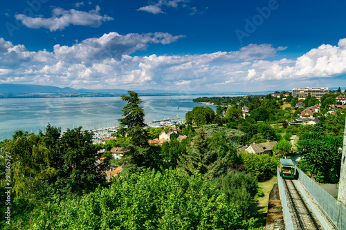 Top view of the green coast and the port of Thonon les Bains, boats, Lake Geneva, and the blue sky with clouds.