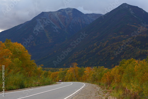 Autumn picturesque road with dark mountains, volcanoes and yellow trees.